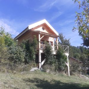Cabane en bois perchée, entourée de verdure, avec balcon et ciel bleu.