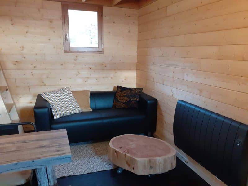 Chalet en bois chaleureux avec canapé noir et table en bois brut.