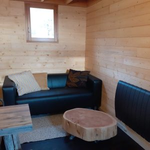 Cabane en bois avec un canapé noir et une table en bois brut, ambiance chaleureuse.