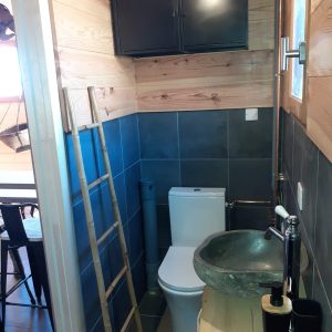 Salle de bain dun hébergement insolite en bois, avec lavabo en pierre et décor moderne.