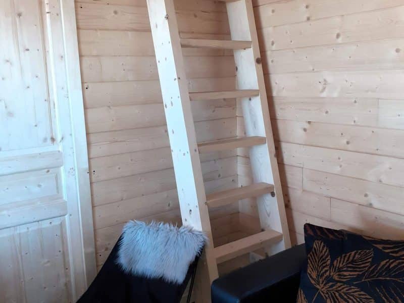 Cabane en bois avec échelle en bois et fauteuil confortable, ambiance chaleureuse.
