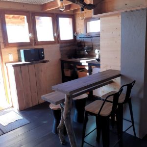 Cabane en bois avec cuisine moderne et table en bois brut, lumineuse et accueillante.