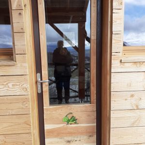 Cabane en bois avec une porte vitrée, offrant une vue panoramique sur la nature.