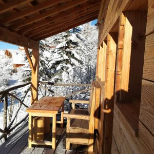 Cabane en bois avec terrasse, entourée de neige, offrant une vue paisible.