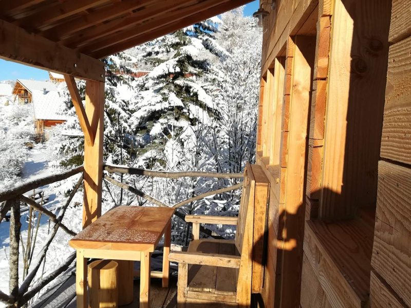 Chalet en bois avec terrasse ensoleillée, vue sur la neige scintillante.