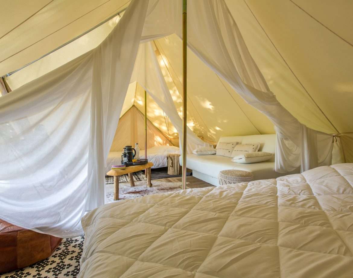 Tente de glamping spacieuse avec literie confortable et décoration chaleureuse.
