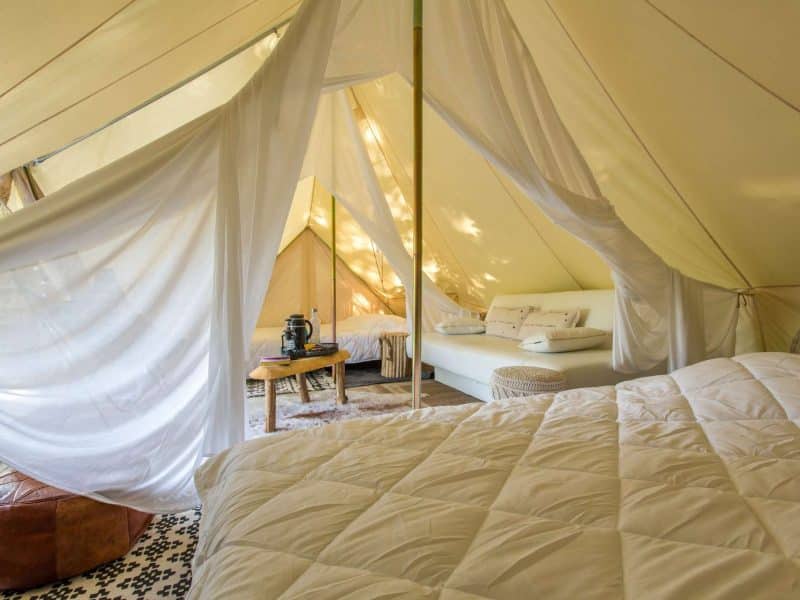 Tente de glamping spacieuse avec literie confortable et décoration chaleureuse.