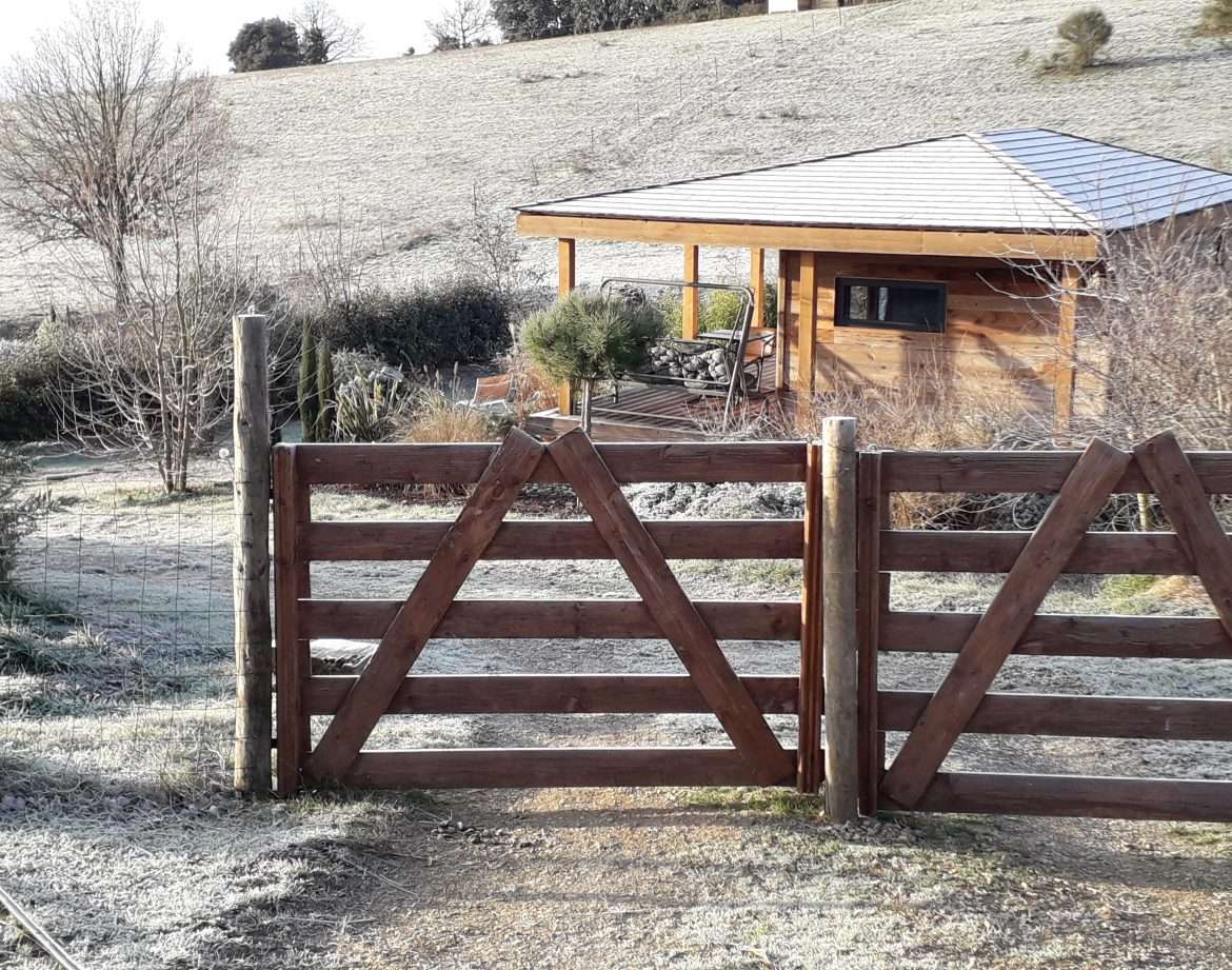 Cabane en bois avec terrasse, entourée de nature et de givre matinal.