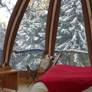 Cabane en bois avec vue sur la neige, lit douillet et ambiance chaleureuse.