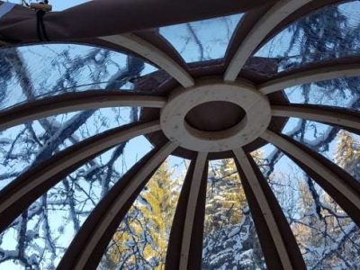Dôme en bois avec un plafond vitré, offrant une vue sur la nature enneigée.