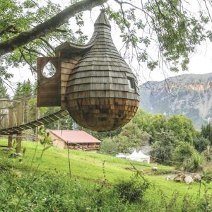 Cabane perchée en bois, suspendue à un arbre, avec vue sur les montagnes verdoyantes.