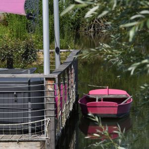 Hébergement flottant avec terrasse, bateau rose amarré au bord de leau.