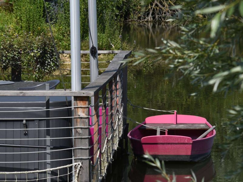 Hébergement flottant avec terrasse, bateau rose amarré au bord de leau.