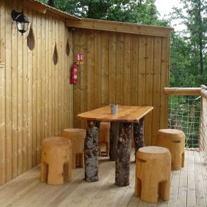 Cabane perchée en Nouvelle-Aquitaine avec terrasse en bois et mobilier en rondins.