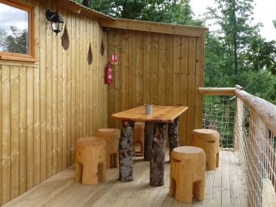 Cabane perchée en Nouvelle-Aquitaine avec terrasse en bois et mobilier en rondins.