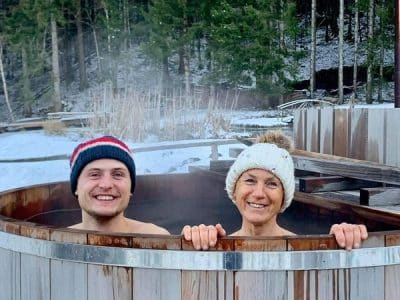 Bain nordique en bois, couple souriant dans un cadre naturel enneigé en Auvergne-Rhône-Alpes.