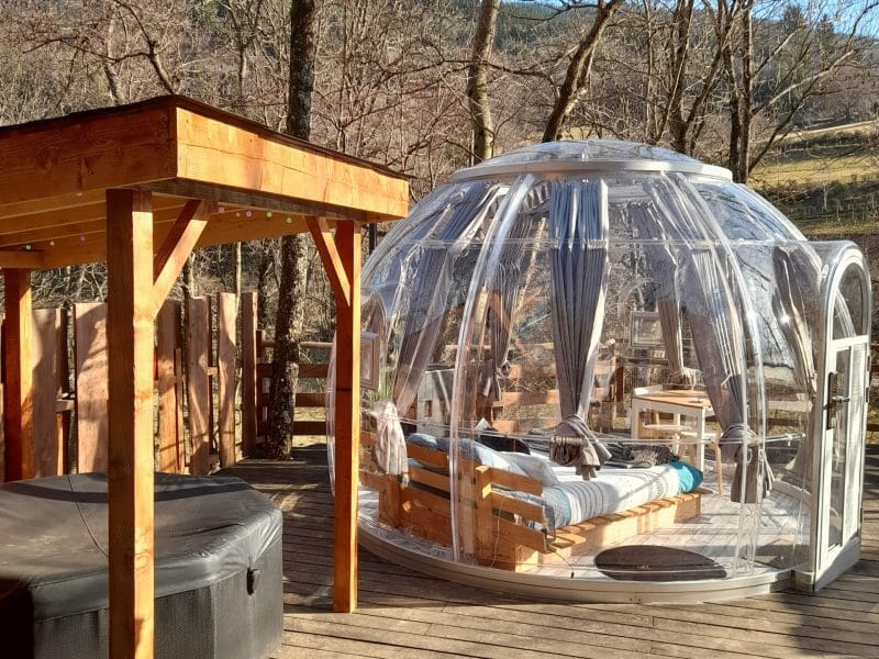 Hébergement insolite en bulle transparente, avec un lit et un coin détente en bois.