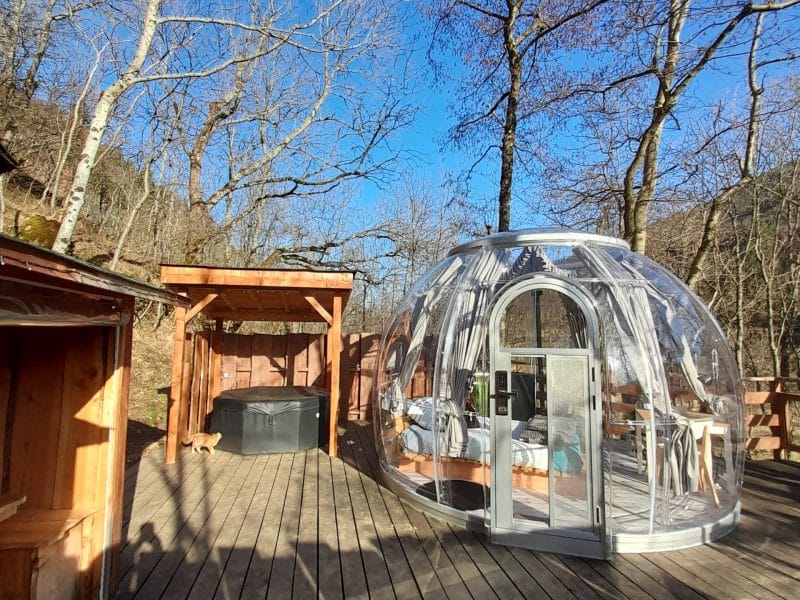 Hébergement insolite : bulle transparente sur une terrasse en bois, entourée darbres.