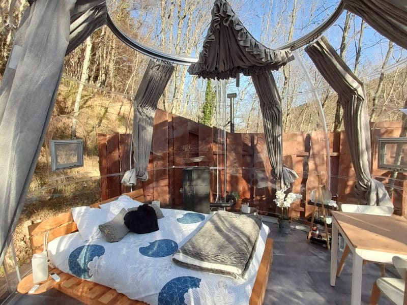 Hébergement insolite : bulle transparente avec lit douillet et décor naturel apaisant.