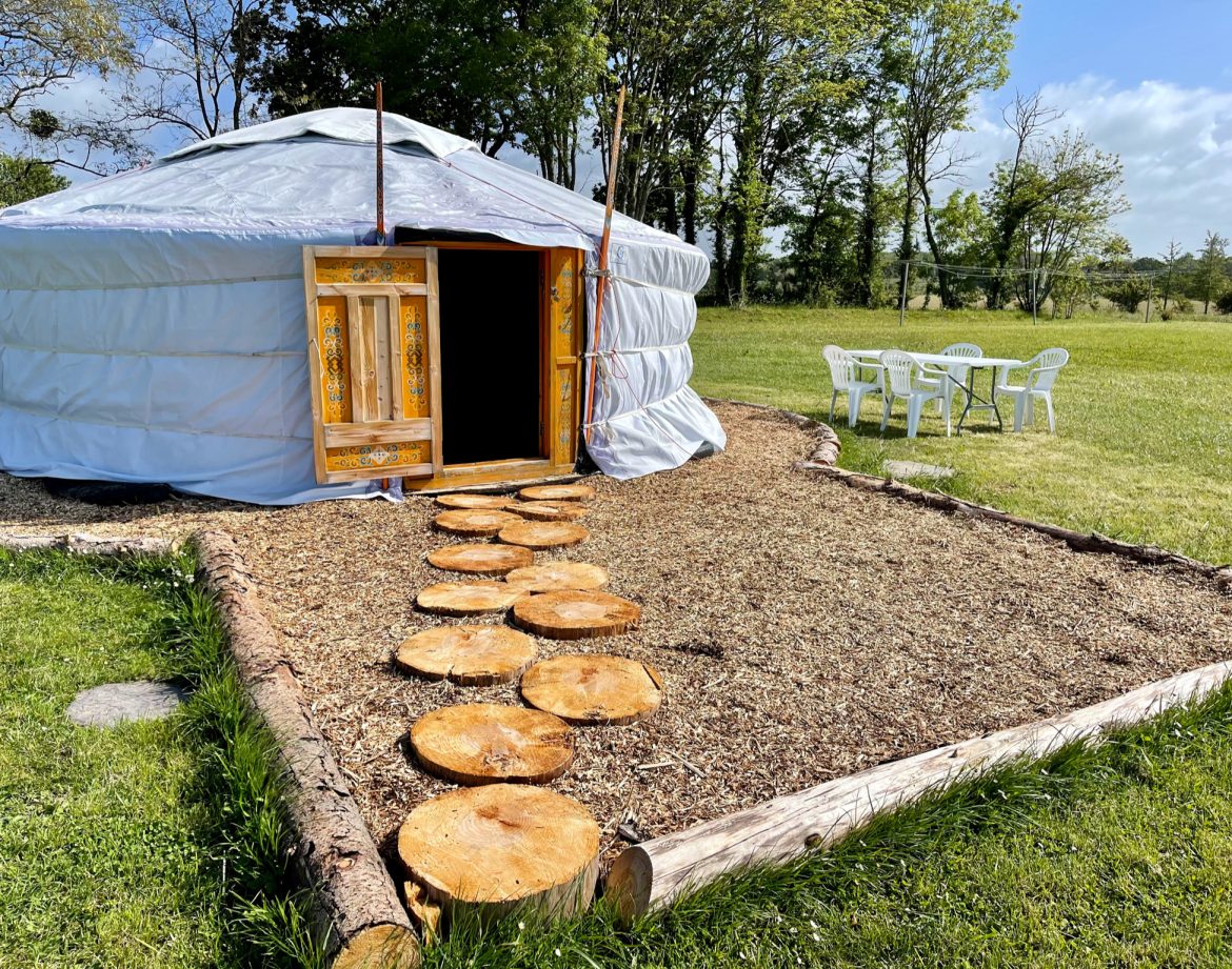 Yourte en Bretagne, avec un chemin de rondins menant à lentrée et des chaises blanches.