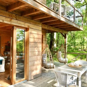 Cabane en bois dans les arbres, avec balançoires suspendues et vue sur la forêt.