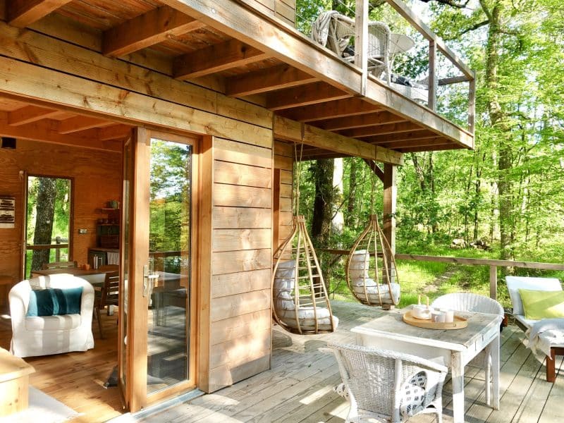 Cabane en bois dans les arbres, avec balançoires suspendues et vue sur la forêt.