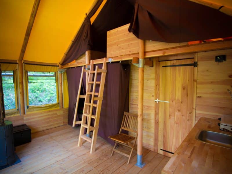 Tente en bois spacieuse avec échelle, poêle et cuisine intégrée. Ambiance chaleureuse.