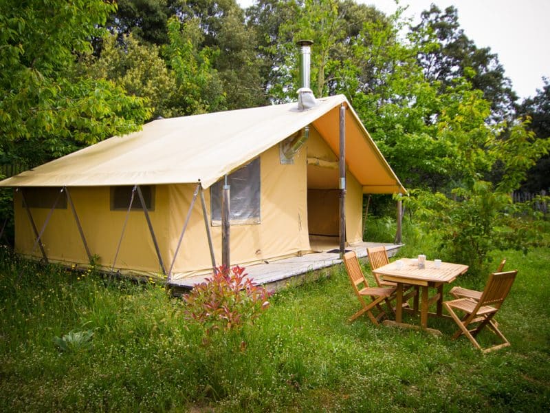 Tente safari spacieuse entourée de verdure, avec une terrasse en bois et mobilier extérieur.