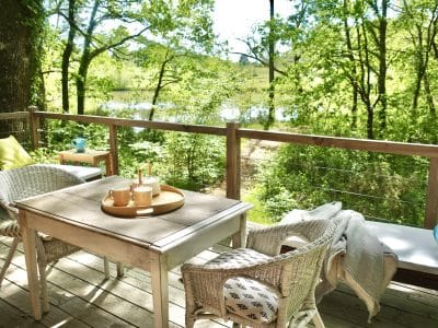 Cabane en bois avec terrasse, vue sur la nature verdoyante et le lac.