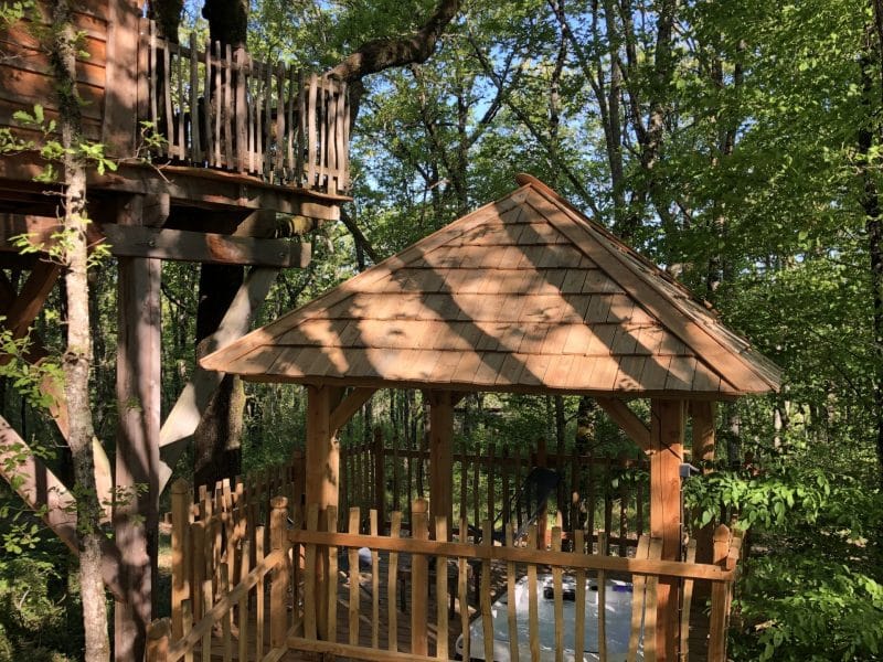 Cabane dans les arbres en Aquitaine, avec un bel espace en bois sous un toit en ardoise.