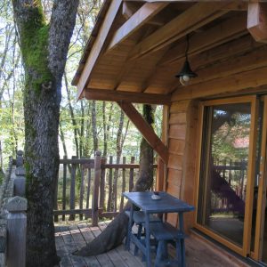 Cabane perchée en bois, avec terrasse en bois et vue sur la forêt verdoyante.