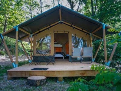 Tente safari en bois, entourée de verdure, avec terrasse et chaises confortables.