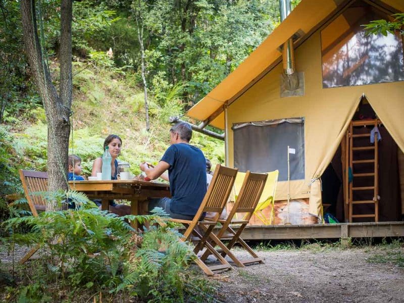 Tente safari confortable en pleine nature, repas en famille autour dune table en bois.