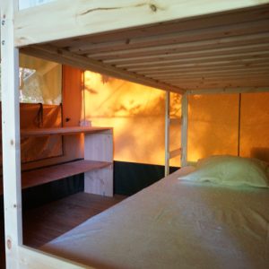 Cabane perchée en bois avec un lit confortable et des lumières chaleureuses.