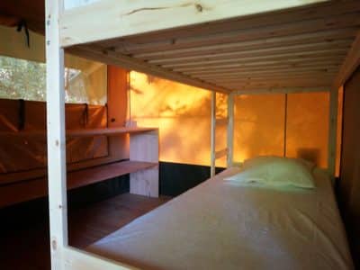 Cabane perchée en bois avec un lit confortable et des lumières chaleureuses.