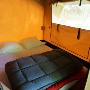 Tente glamping cosy avec lit douillet et lumière chaleureuse à Languedoc-Roussillon.