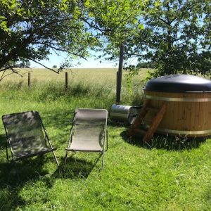 Hébergement insolite : un jacuzzi en bois dans un jardin verdoyant, avec chaises longues.