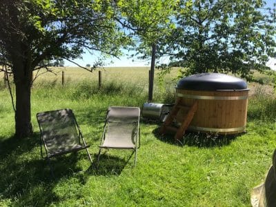 Hébergement insolite : un jacuzzi en bois dans un jardin verdoyant, avec chaises longues.