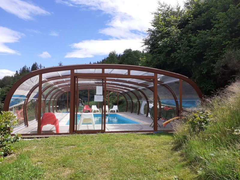 Gîte avec piscine couverte, entouré de verdure et de chaises colorées.