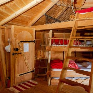 Cabane en bois avec lits superposés et une mezzanine en filet, ambiance chaleureuse.