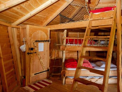 Cabane en bois avec lits superposés et une mezzanine en filet, ambiance chaleureuse.
