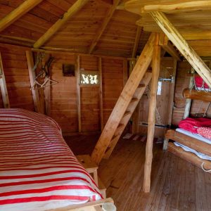 Cabane en bois avec lits superposés et décor chaleureux en rouge et blanc.