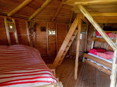 Cabane en bois avec lits superposés et décor chaleureux en rouge et blanc.