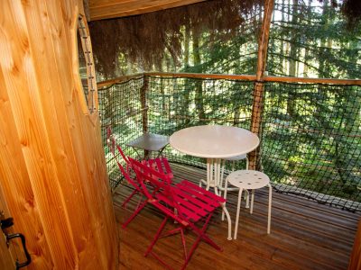 Cabane perchée en Auvergne avec terrasse en bois et chaises colorées.