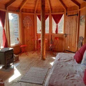 Cabane en bois ronde en Auvergne, avec un poêle et des chaises rouges.