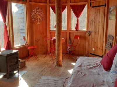 Cabane en bois ronde en Auvergne, avec un poêle et des chaises rouges.