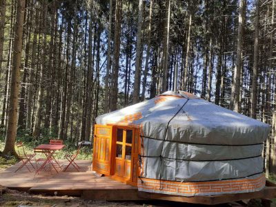 Yourte colorée en bois, nichée dans la forêt dAuvergne, avec une terrasse accueillante.