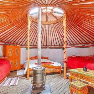 Yourte colorée en Auvergne, avec lits orange et poêle central chaleureux.