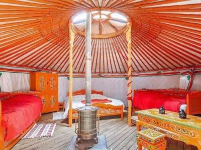 Yourte colorée en Auvergne, avec lits orange et poêle central chaleureux.