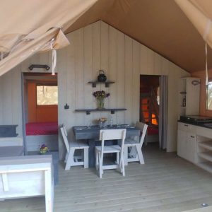 Hébergement insolite en tente lodge, intérieur lumineux avec cuisine et coin salon.